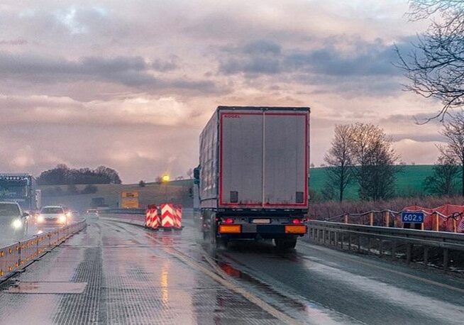 A truck driving down the road on wet pavement.